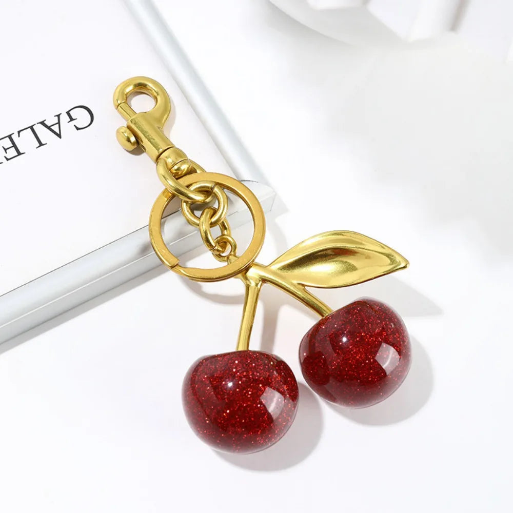 Gold keychain with red cherry-like charms on a white background